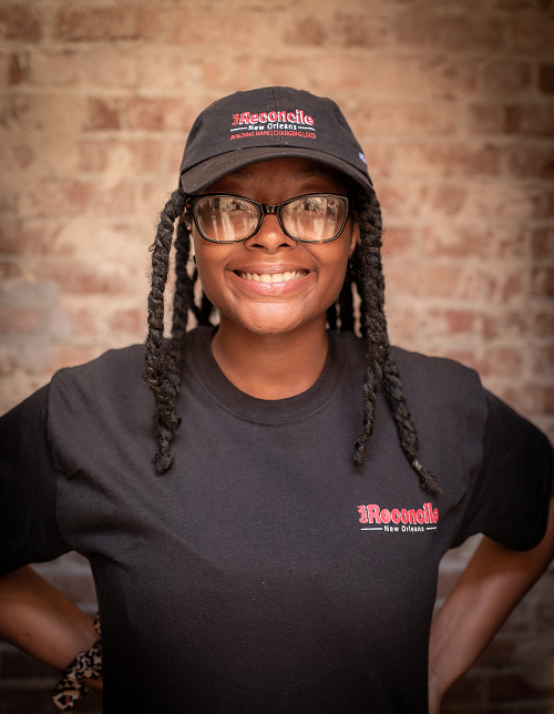 Brianna, a graduate of the STRIVE Future Leaders program, faces the camera smiling and wearing a Cafe Reconcile baseball cap and black t-shirt