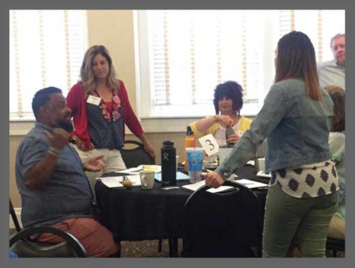 Several people engage in discussion around a table.