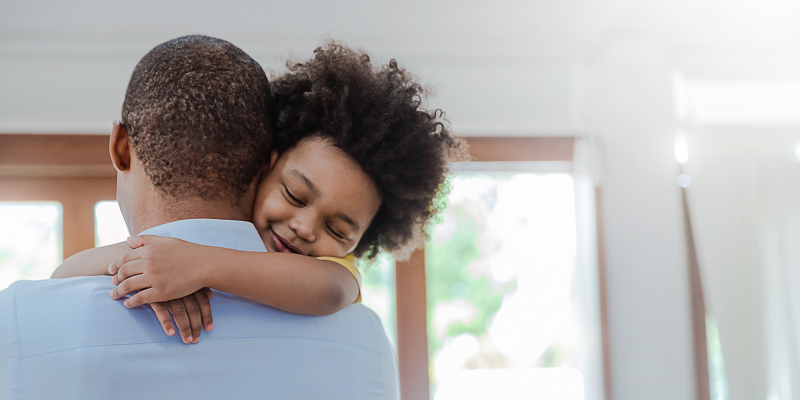 A young girl hugs her father around the neck.