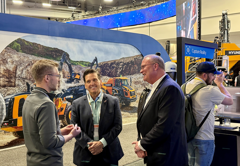Several men speak in front of a construction display at an industry expo.