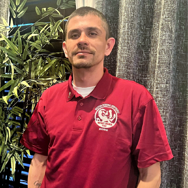 A man in a red tee shirt smiles at the camera.