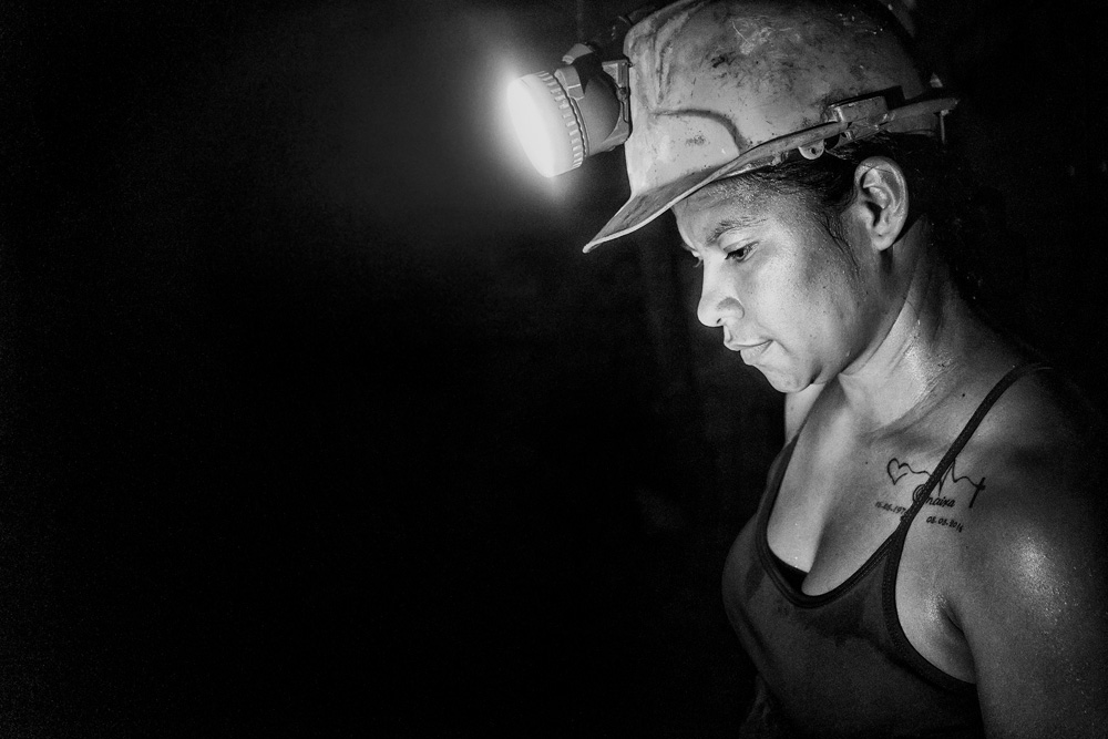 A female worker wears a helmet and a headlamp in the darkness in this black and white photo.  