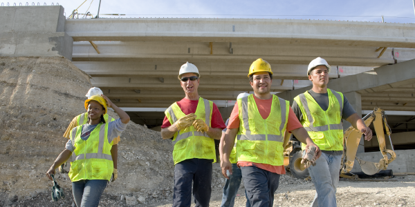 Construction workers in safety gear walk away from a construction site.