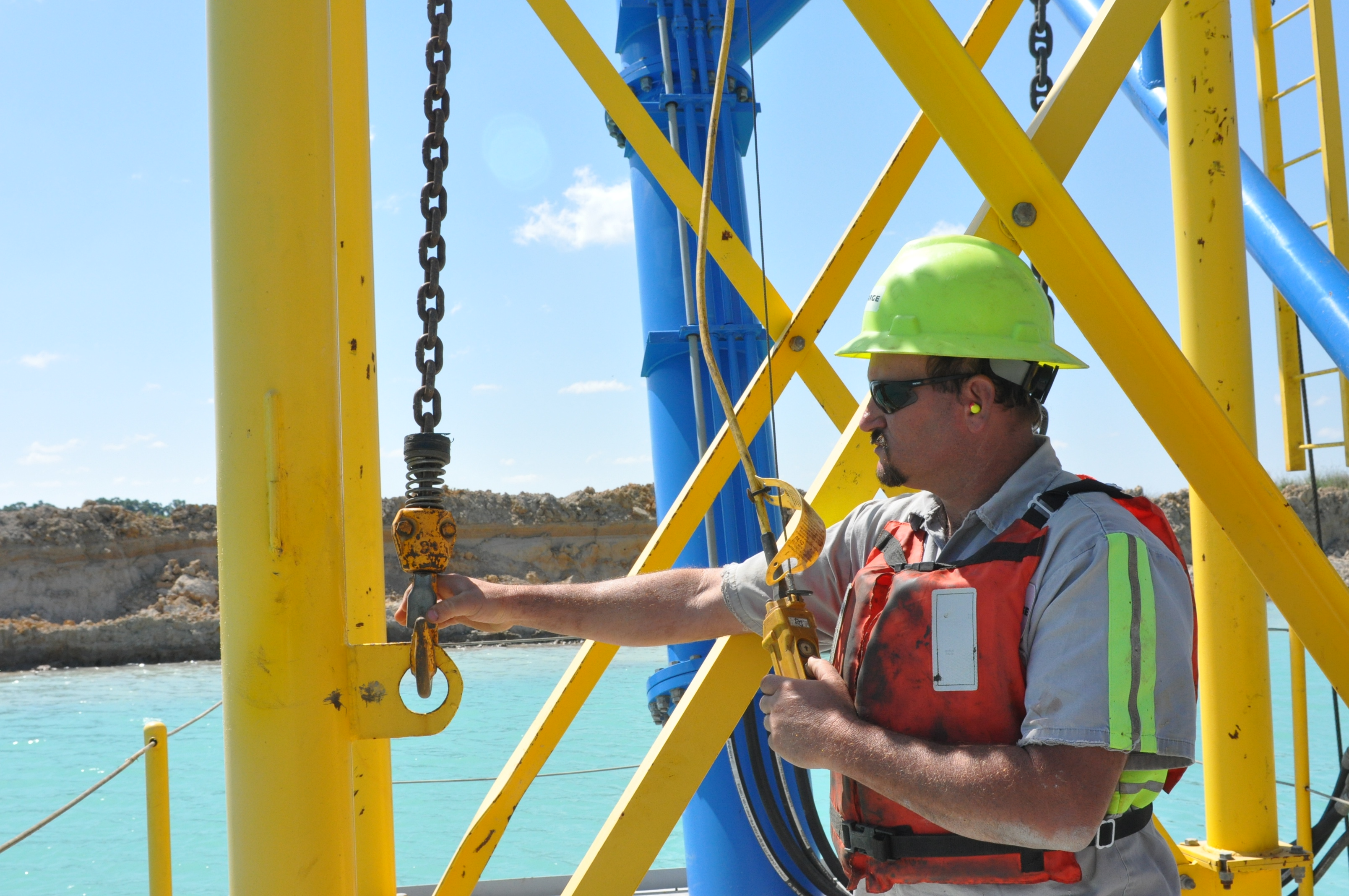 A miner stands on equipment during a sunny day at a surface mine