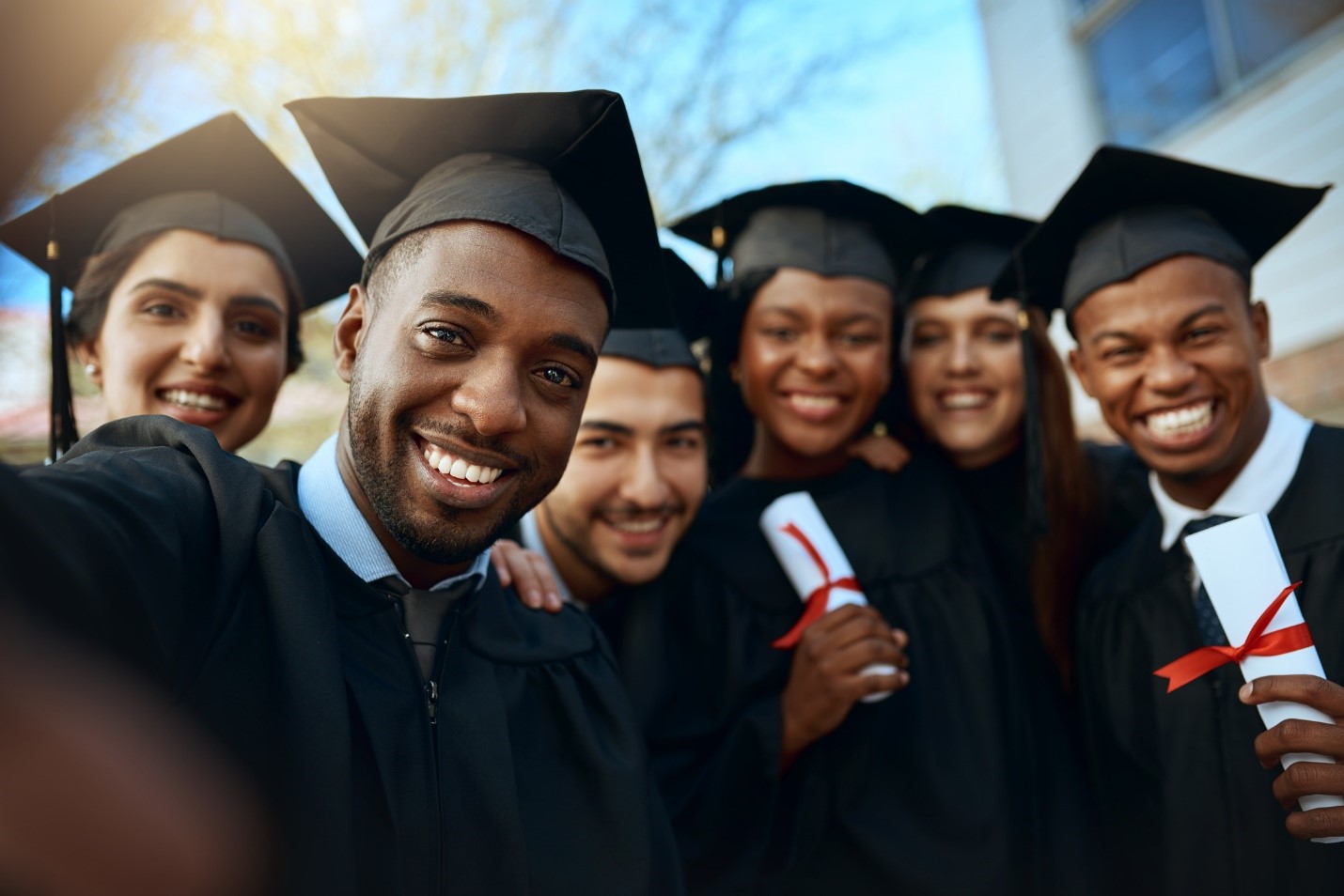 Six graduates taking a selfie while wearing their black graduation robes and hats