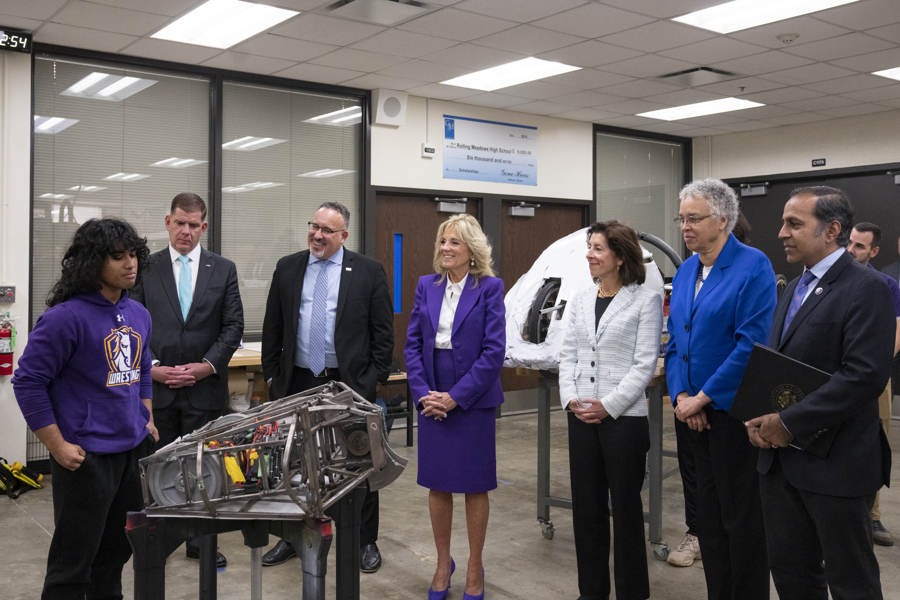 A student displays a rudimentary robot to several adults, including Secretary Walsh and First Lady Jill Biden. 