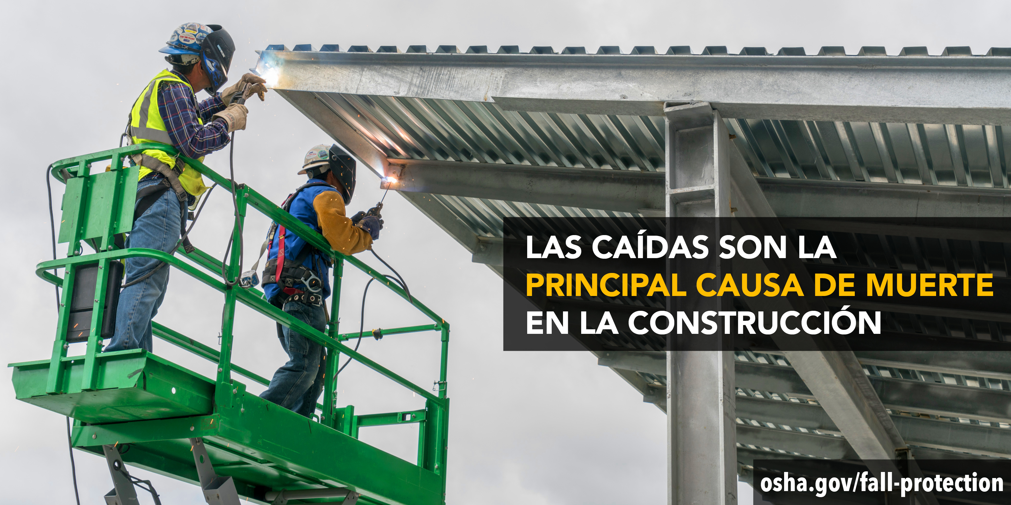 Dos trabajadores se paran en una plataforma elevada para soldar un techo de metal. Llevan puestos arneses de protección contra caídas, cascos para soldar, guantes y ropa de alta visibilidad. Las caídas son la principal causa de muerte en la construcción. osha.gov/fall-protection