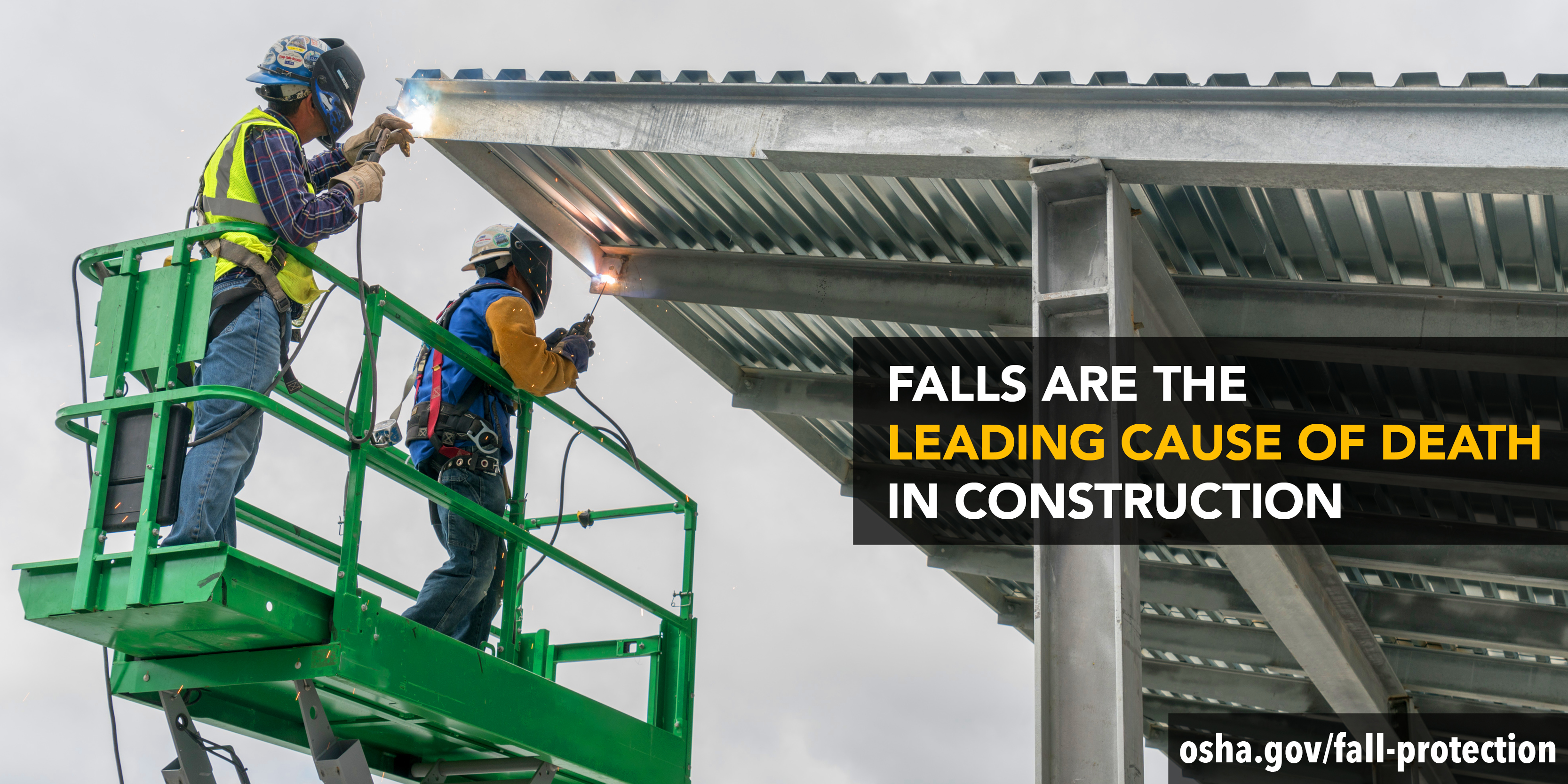 Two workers stand on an elevated platform to weld a metal roof. They are wearing fall protection harnesses, welding helmets, gloves and high visibility clothing. Falls are the leading cause of death in construction. osha.gov/fall-protection