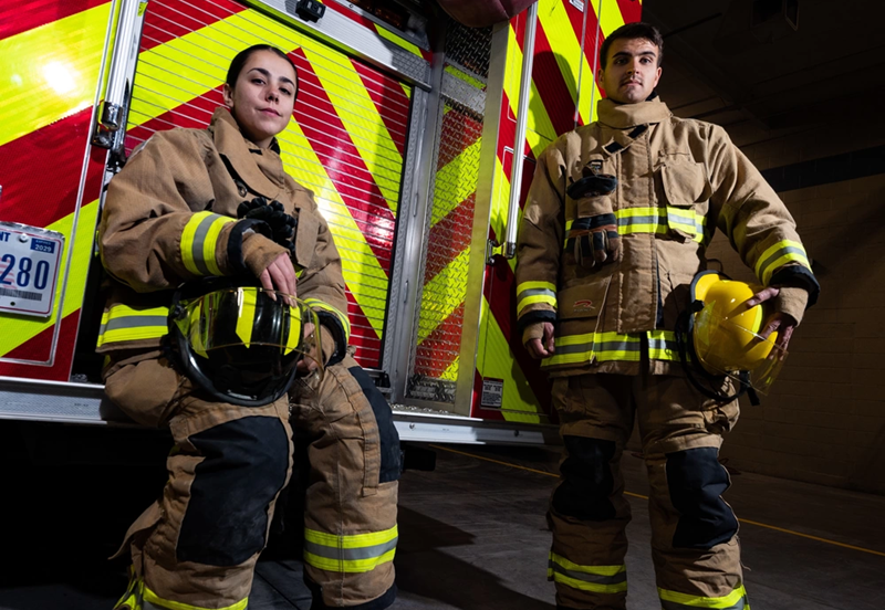 Wearing firefighting gear, Airman 1st Class Nicolette Chilson and Airman 1st Class William Phelp stand in front of a firetruck at Nellis Air Force Base, Nevada. Nellis fire protection specialists are trained to deal with a variety of scenarios, such as natural fires, burning rocket fuel and hazardous material fires. U.S. Air Force Photo by Airman 1st Class Trevor Bell. 
