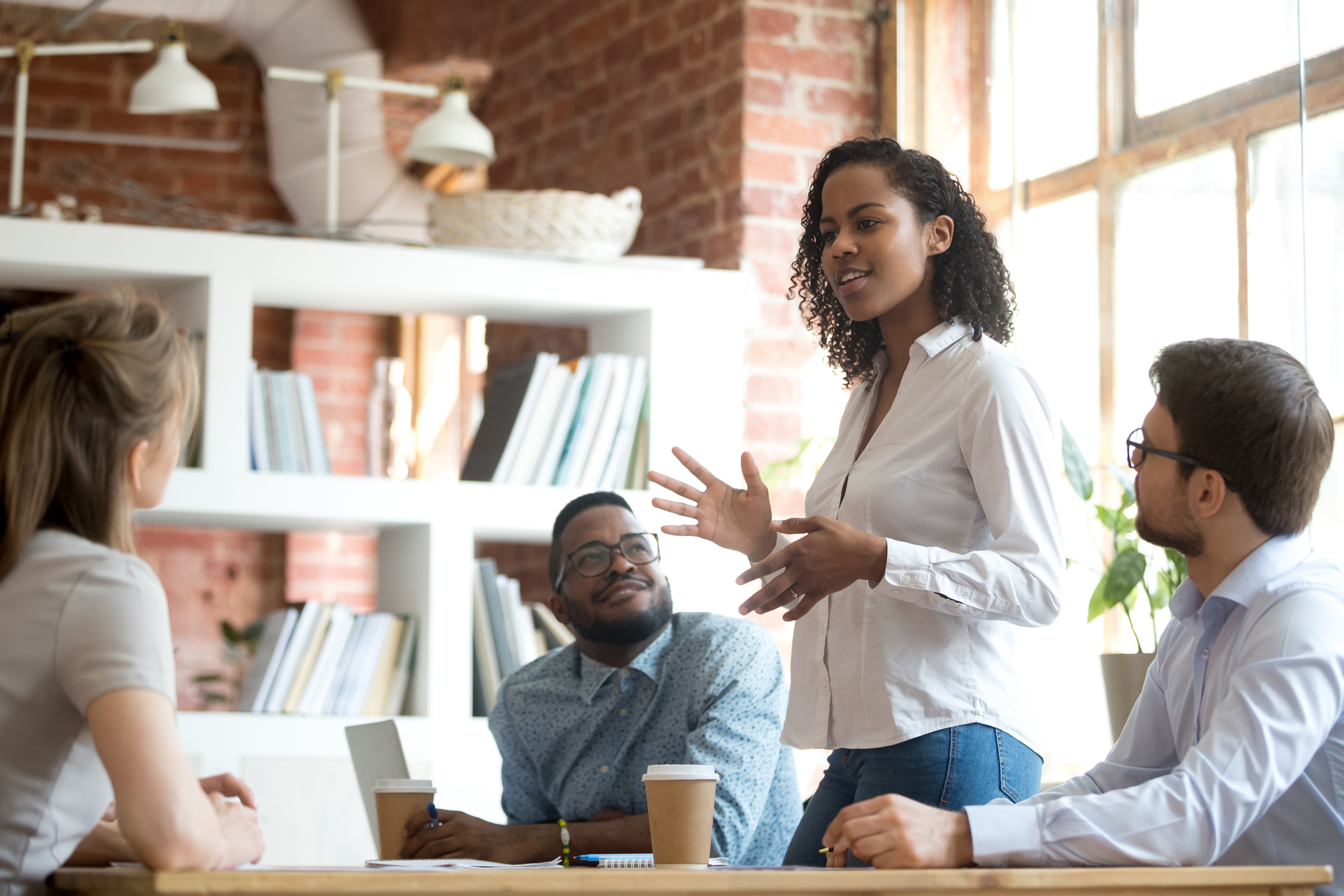 Female employee standing and speaking to seated colleagues