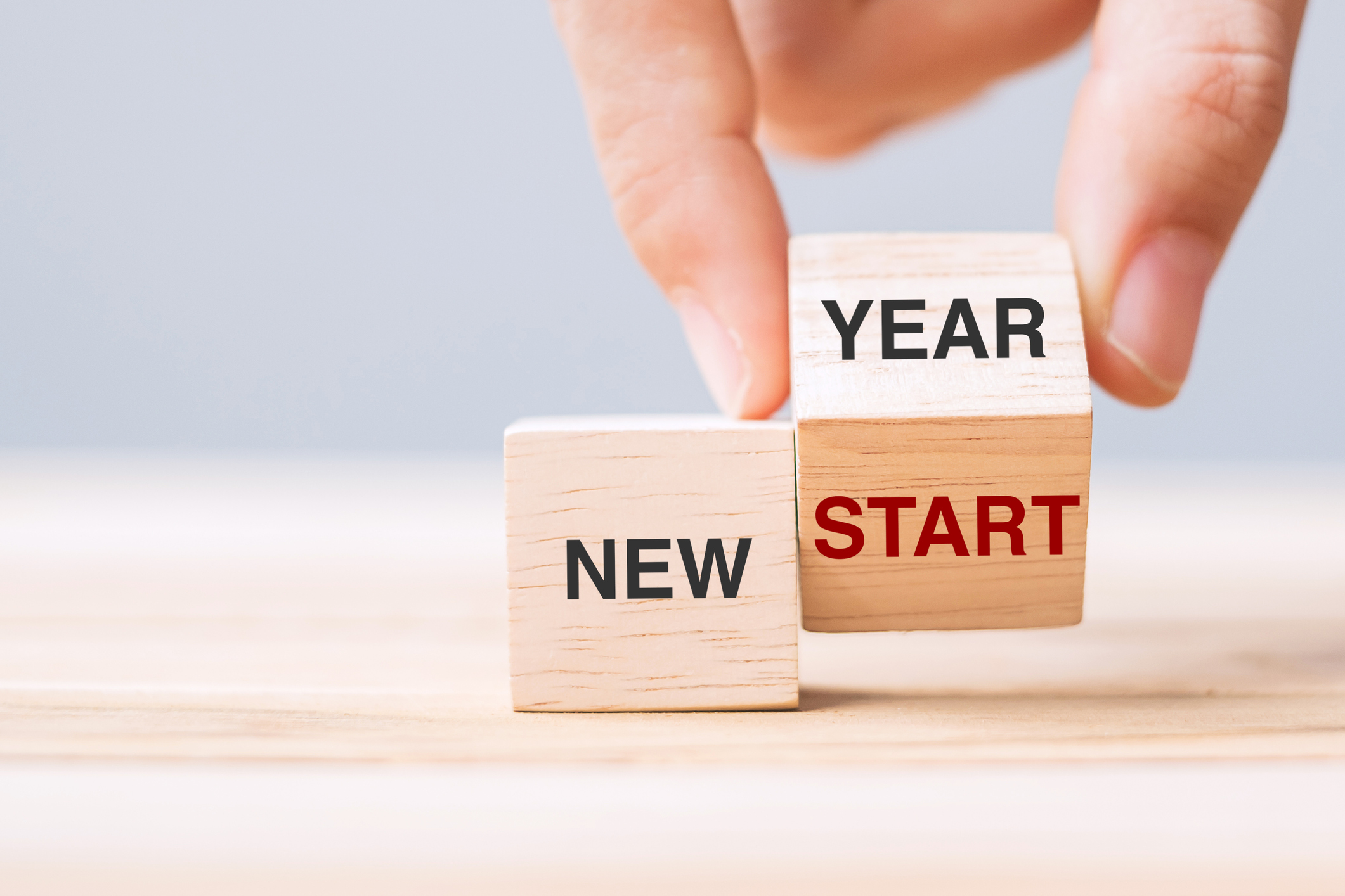 A hand placing two blocks on top of each other that read New Year New Start