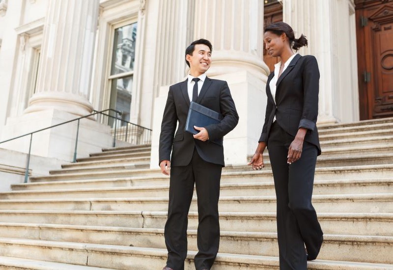 A man and a woman in professional dress walk down the steps of a government building.