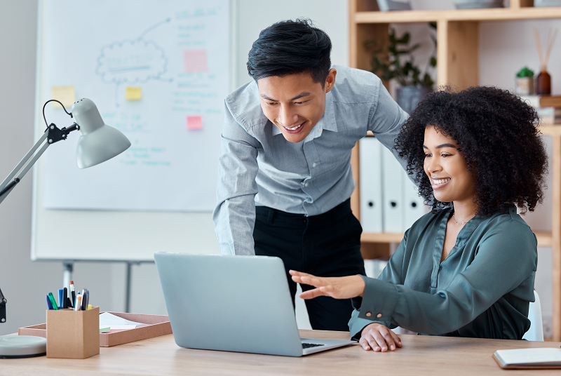 Two co-workers look at a computer in an office environment.