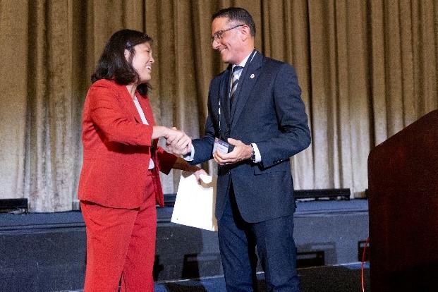 A woman in a red suit shakes hands with a man in a blue suit on a stage.