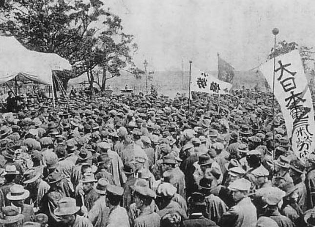 A black and white photo of a tightly packed crowd of workers carrying signs in Japanese listening to a speech.