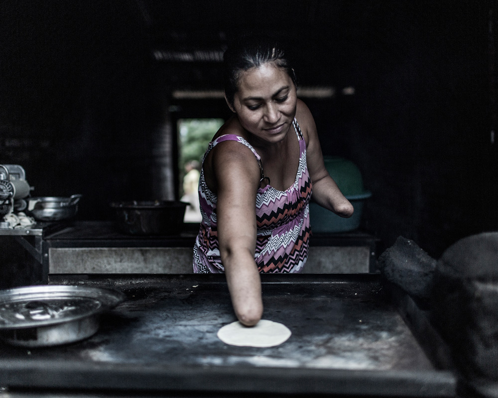 A woman who does not have hands places a tortilla on a cooktop.