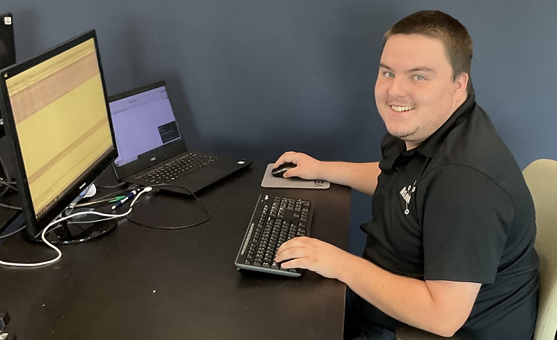 A young man working on a computer pauses to smile at the camera.