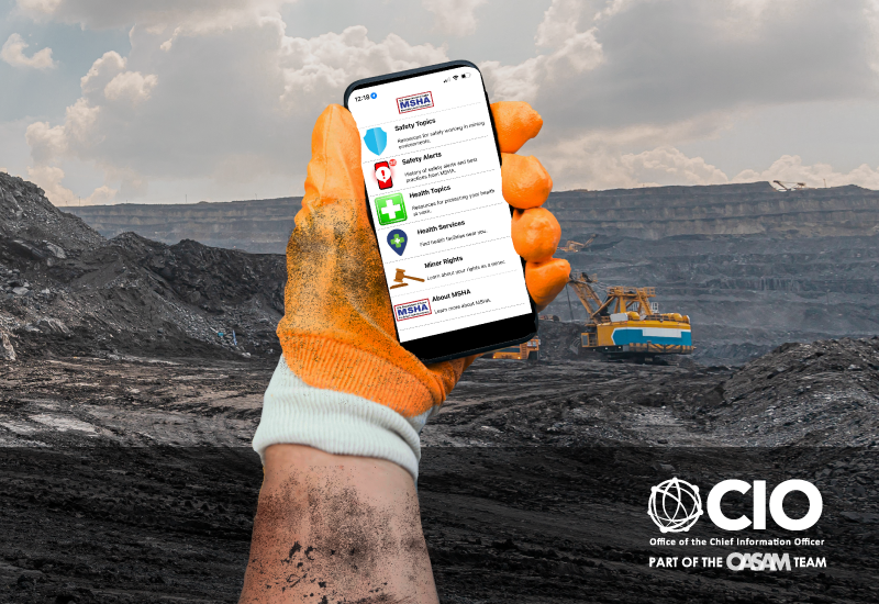 Wearing a work glove, a miner’s hand can be seen holding a mobile device and using the MSHA Safety + Health App.