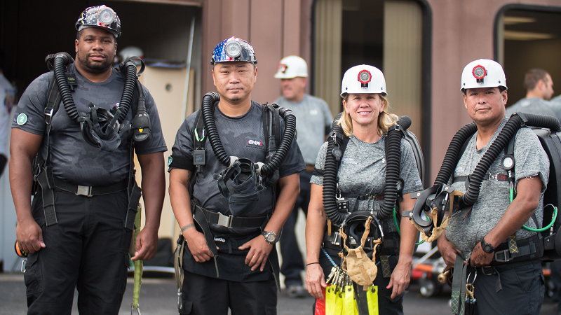 Four diverse members of a mine rescue team wearing hardhats and other safety gear