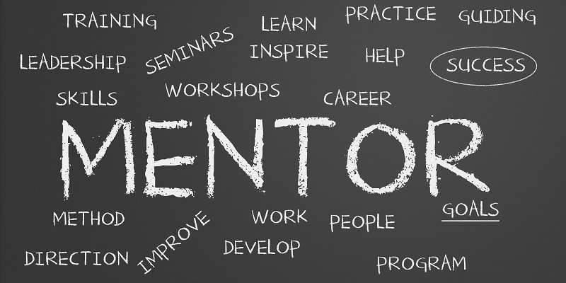 The word MENTOR written on a blackboard, surrounded by related words like coach, training, leadership, etc.