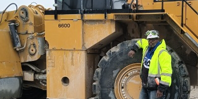 A construction worker with a hard hat stands in front of a large construction vehicle.