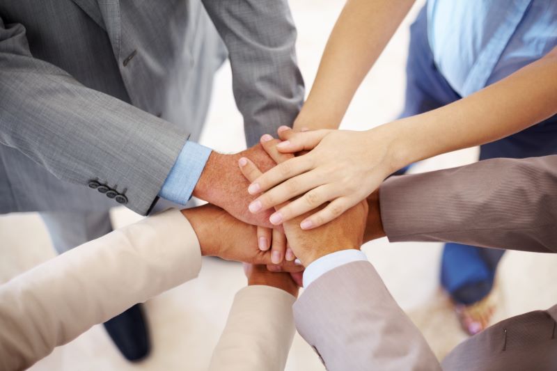 Group of colleagues dressed in various business casual attire joining hands in the middle to show unity. 