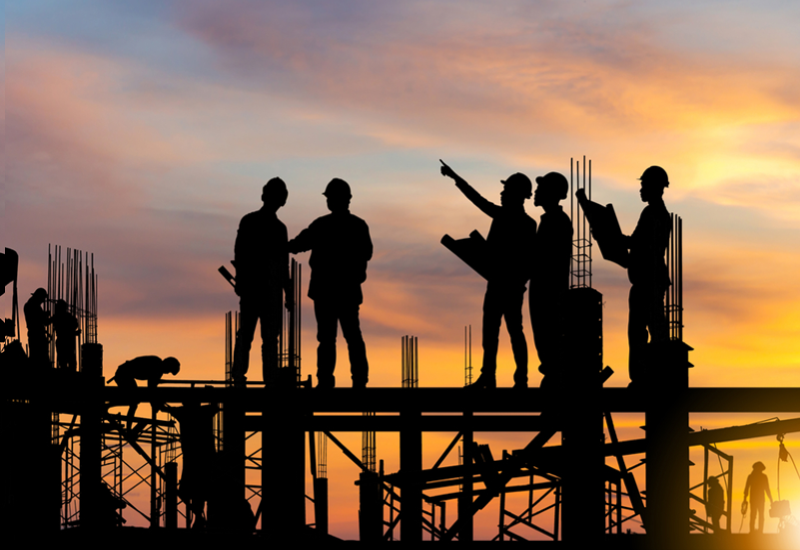 Silhouettes of construction workers standing on scaffolding as the sun sets behind them
