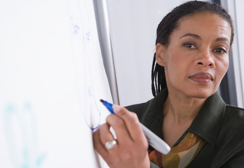 An older Black woman in professional dress looks at the camera while holding a marker. 