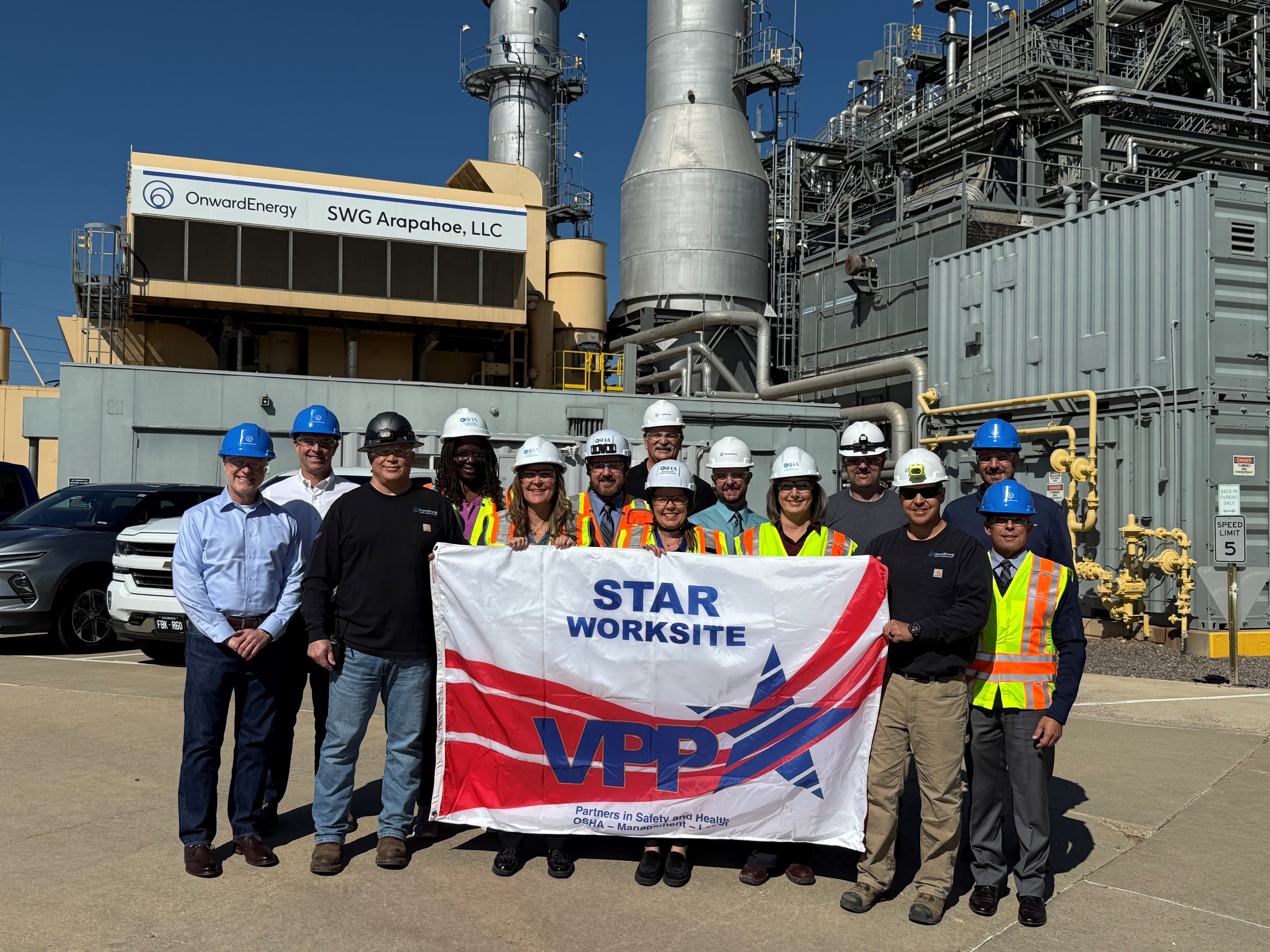 A group of people in hardhats stand in front of an energy plant holding a banner that says "STAR Worksite, VPP"