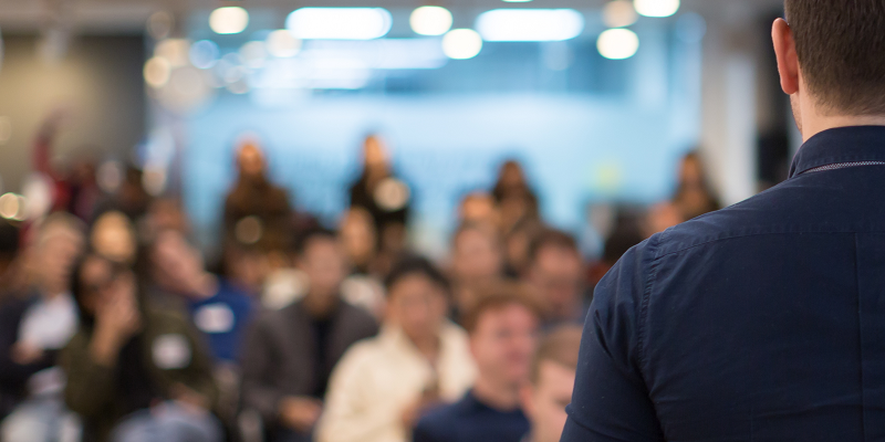 The back of a male speaker as he addresses an audience