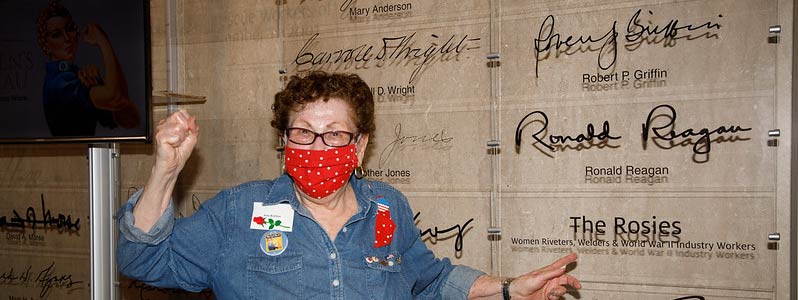 June Robbins points to the Rosies entry in the Labor Hall of Honor while standing by a Rosie the Riveter poster
