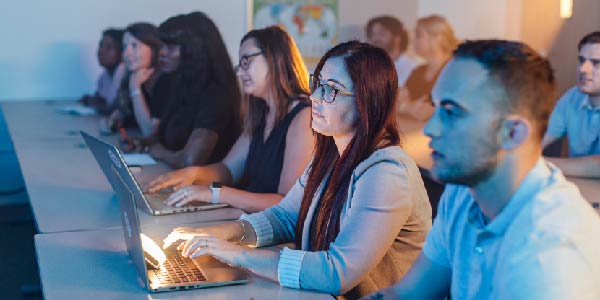 Photo of students in a classroom, with computers set up on the tables in front of them.