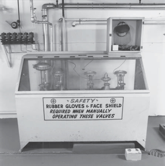 A close-up of T-Plant Valves at the Hanford Site. They are contained within a box that has a glass top. A sign on the box says "Safety: Rubber gloves and face shield required when manually operating these valves."