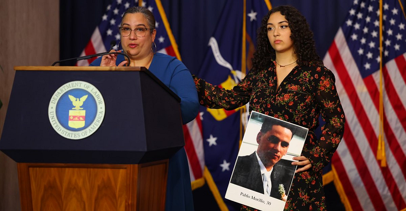 Wanda Engracia speaks at a podium. Her 18-year-old daughter Samatha stands beside her, holding a photo of her deceased father, with a hand on her mother's shoulder.