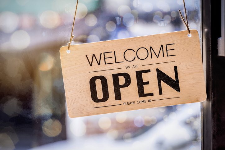 A sign hangs in a shop window that says "Welcome, we are open, please come in"