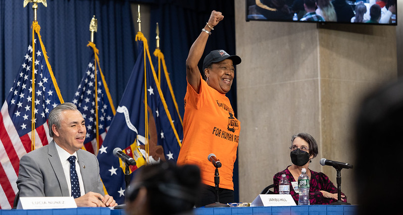 A woman wearing an orange shirt stands and gestures enthusiastically during a panel discussion at the Workers’ Voice Summit.