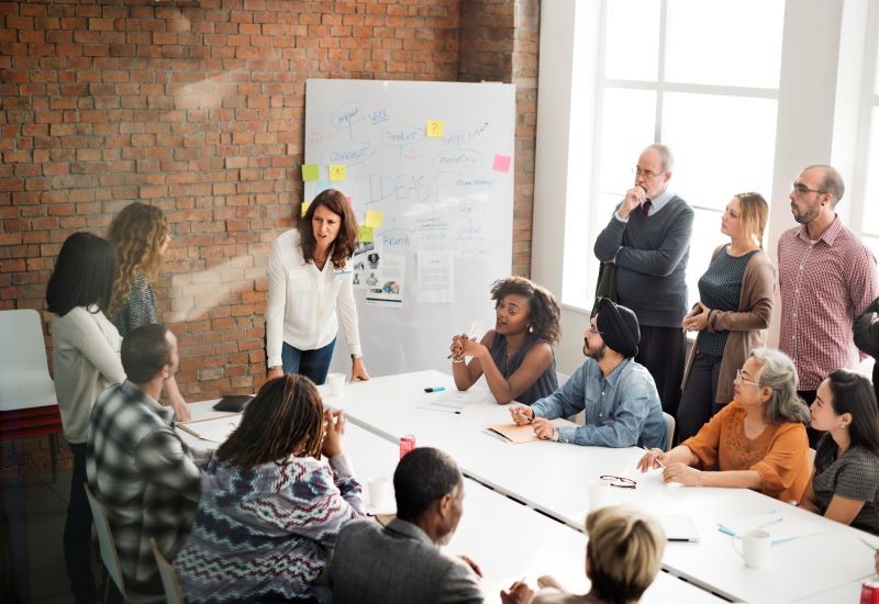 A woman speaking to a group of workers seated at a conference table.