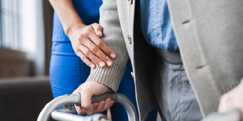 A healthcare worker assists an older man using a walker