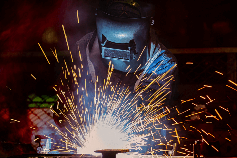 A welder with a protective face mask works, causing sparks to fly