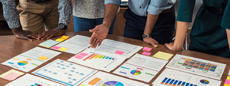 Coworkers look at charts spread out on a table