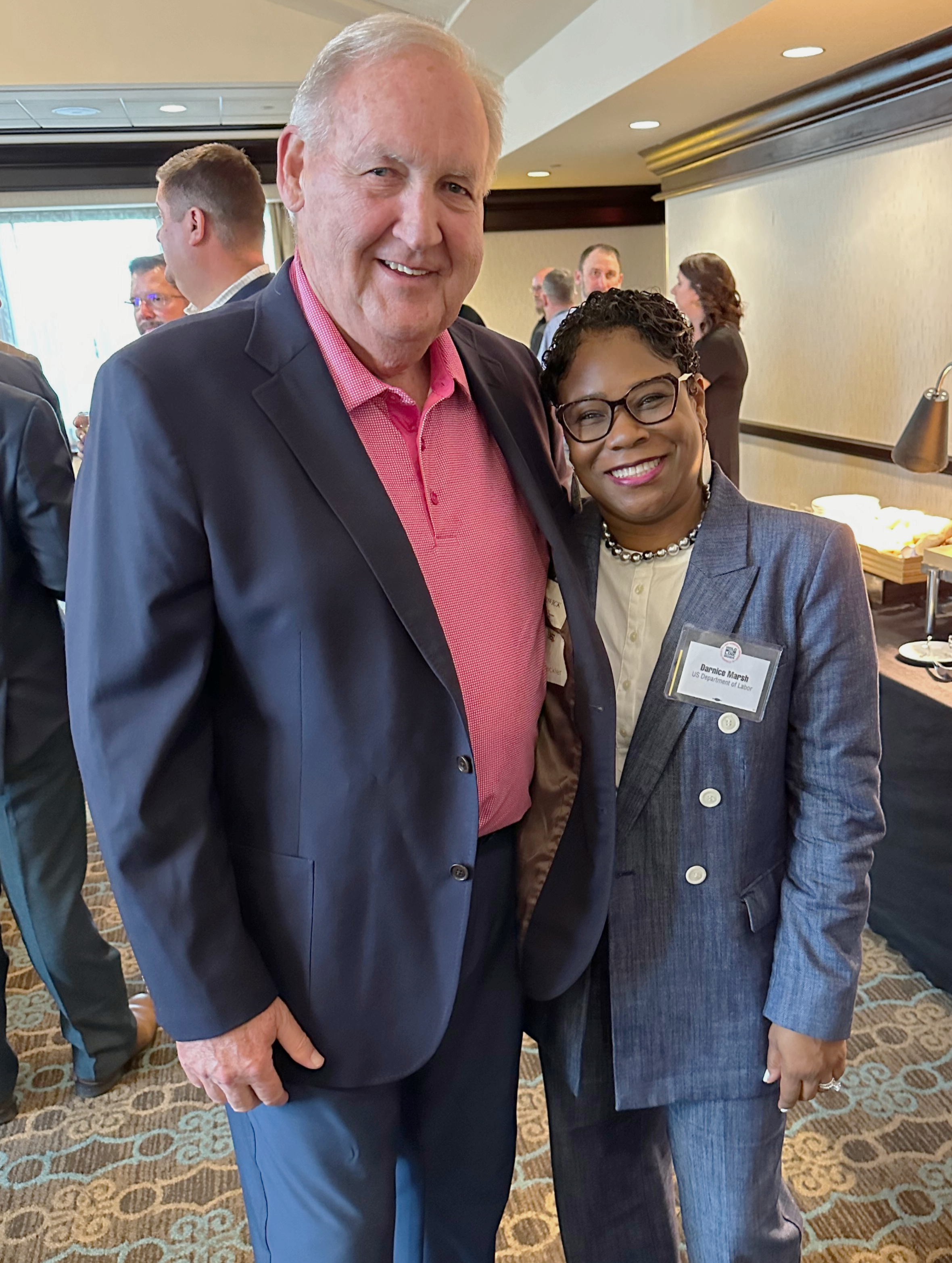 A man and a woman in a conference center pose for a photo.