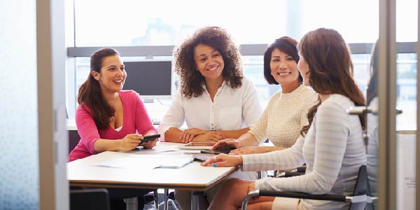 A diverse group of professional women gathered around a conference table. 