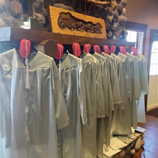 Graduation gowns hang in front of a fireplace.