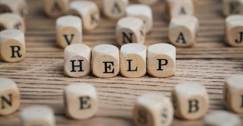 Small alphabet blocks are scattered across a table. In the center, four blocks spell out the word “help.”