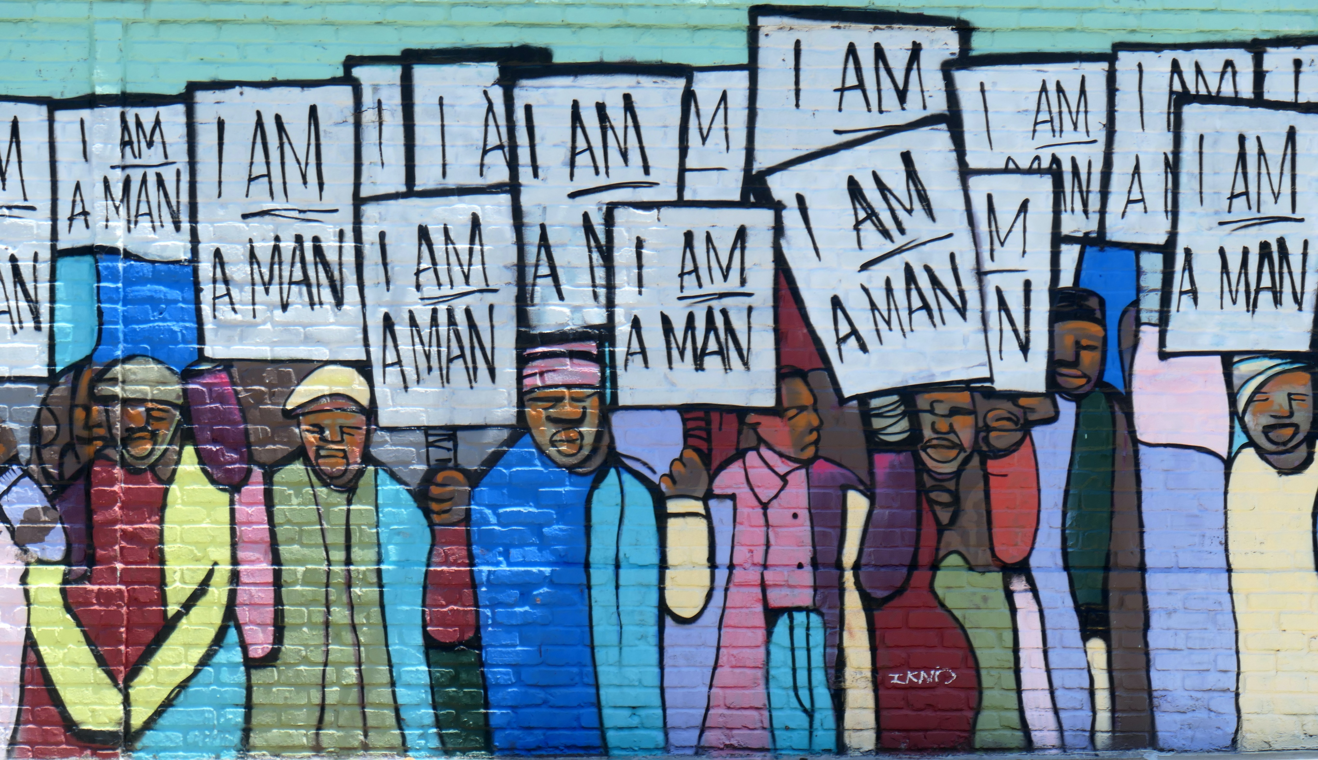 Colorful mural recreating a 1968 black and white photograph of Black workers in Memphis holding signs that read "I am a man"