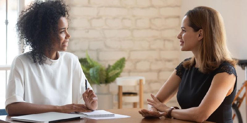 A boss and employee, both women, sit at a table and discuss accommodations.