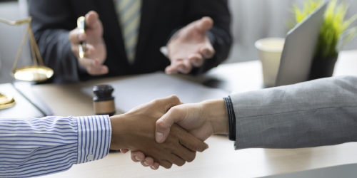 Two people shake hands while seated at a table. A mediator is visible behind them. 