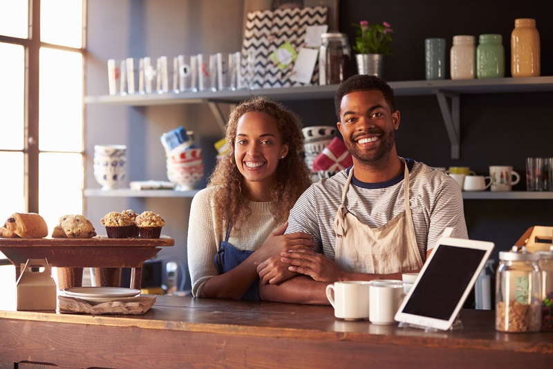 Two coffeeshop workers smiling and leaning on the counter. 