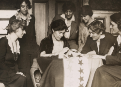 National Woman's Party activists watch Alice Paul sew a star onto the NWP Ratification Flag, representing another state's ratification of the 19th Amendment.