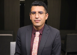 A man in suit and tie sits at a table in a conference room.